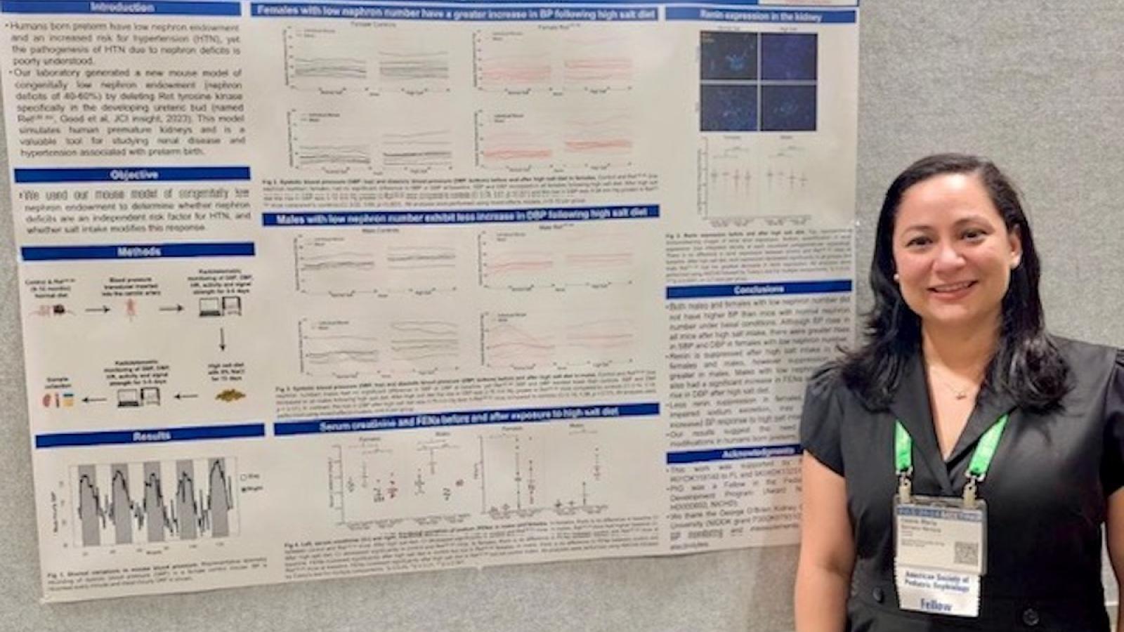 A nephrology fellow standing in front of her research poster at a conference.