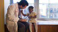 A doctor lets a young patient use his stethoscope.